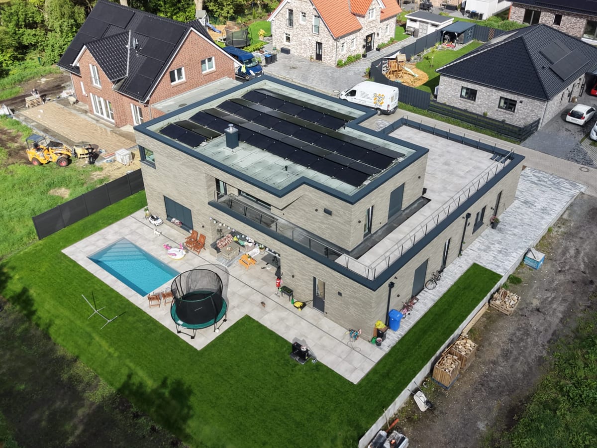 Luftaufnahme der fertigen Aussenanlage: grossformatige Terrassenplatten, eingelassenes Schwimmbecken und angelegte Rasenflaeche an einem Klinkerhaus