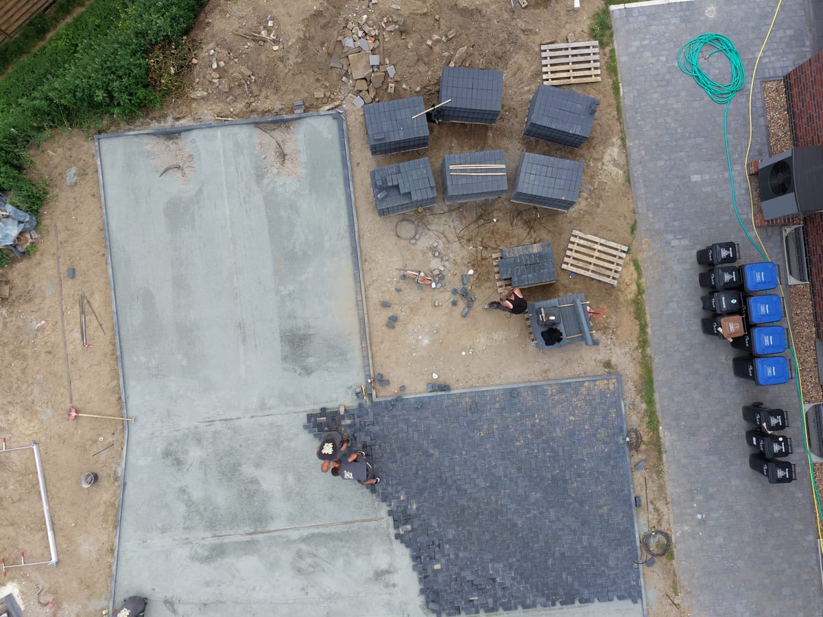 Senkrechte Luftaufnahme der Baustelle mit abgezogener Tragschicht, gestapeltem Pflaster und begonnener Flaeche