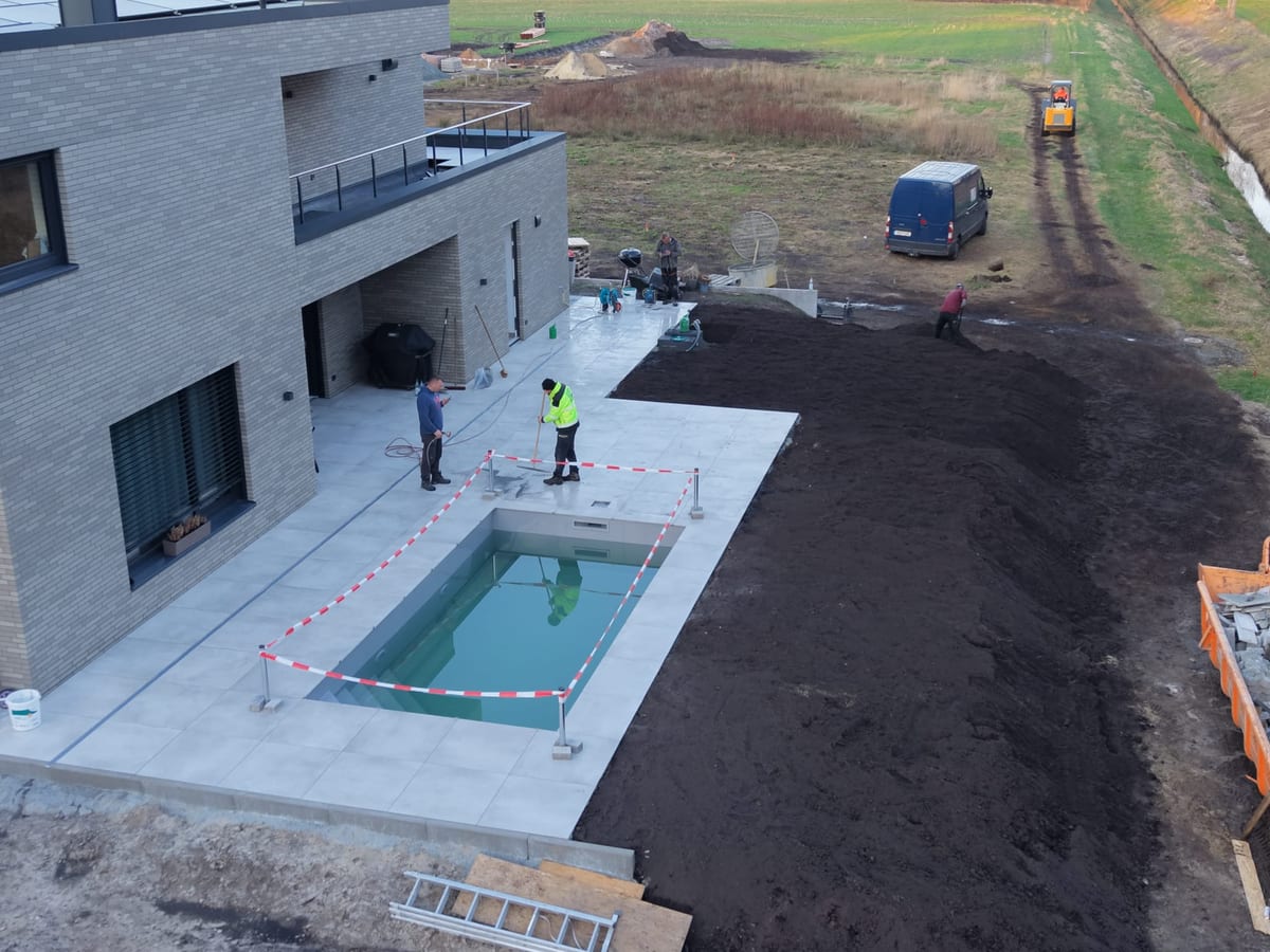 Luftaufnahme: fertige Terrasse mit Schwimmbecken, daneben laufende Erdarbeiten mit Radlader