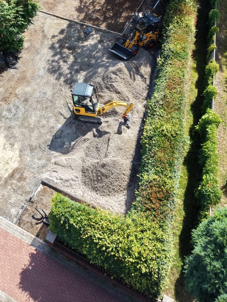 Luftaufnahme: abgezogenes Planum einer Hofflaeche mit Splittmieten, Minibagger und Radlader