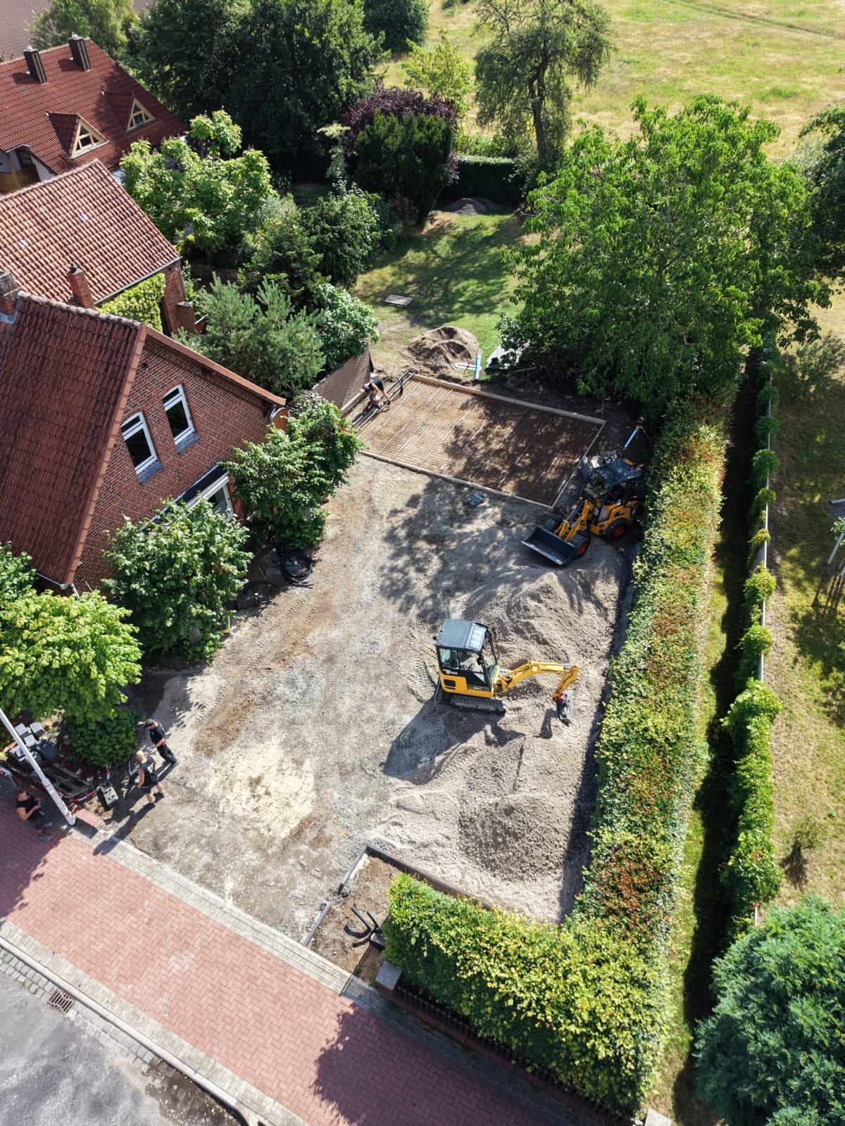 Luftaufnahme: abgezogenes Planum einer Hofflaeche zwischen zwei Wohnhaeusern, Minibagger und Radlader im Einsatz