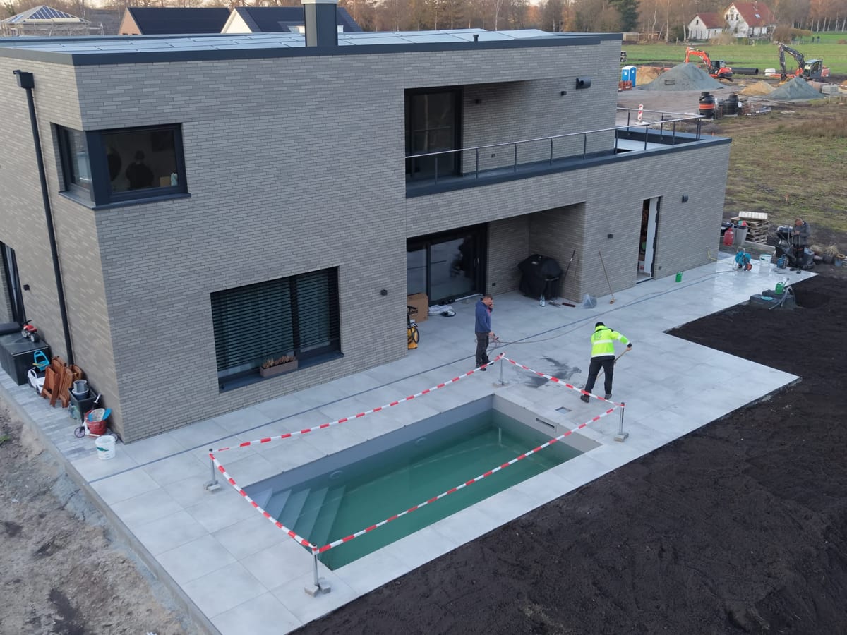 Becken mit Absperrung vor der Klinkerfassade, ringsum die fertig verlegte Plattenflaeche, zwei Arbeiter bei der Endreinigung