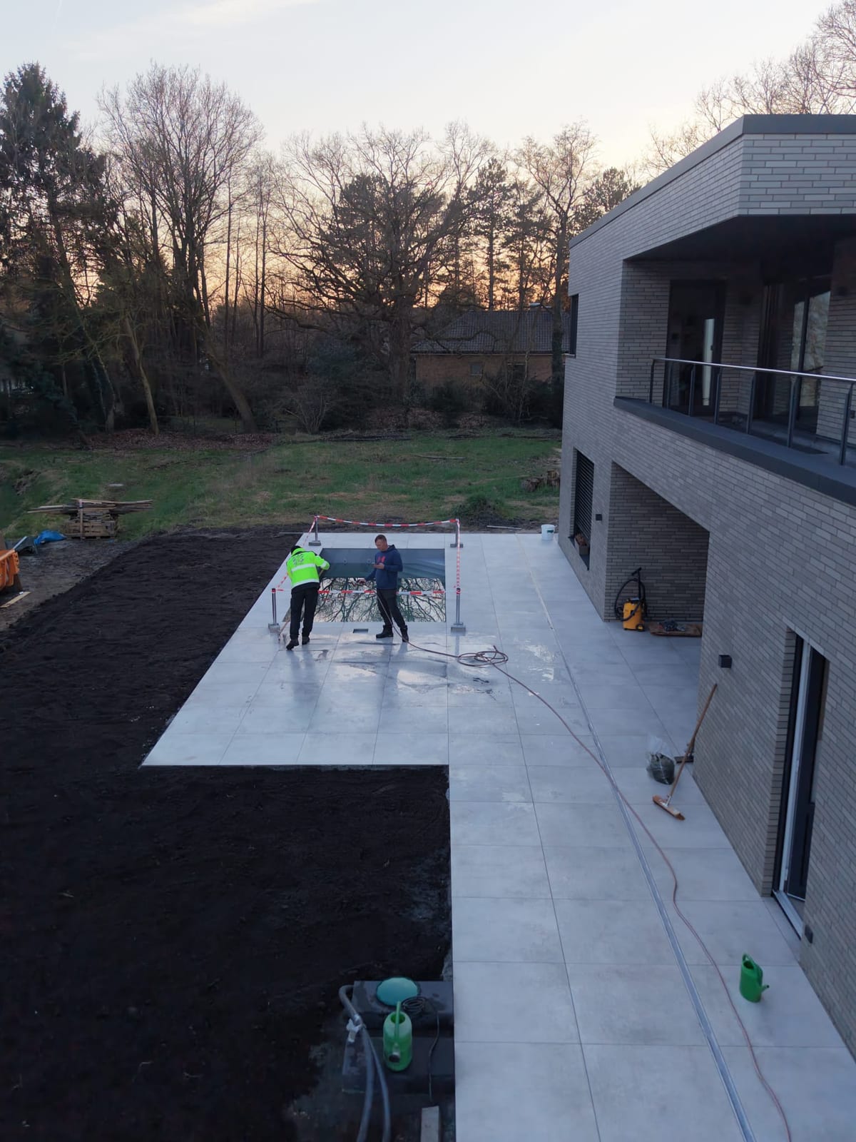 Abendaufnahme aus erhoehter Perspektive: fertig verlegte Terrassenflaeche, abgesperrtes Becken und angrenzende Mutterbodenflaeche