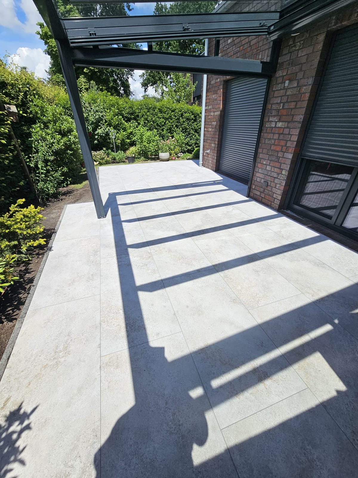 Fertige Terrasse aus hellen grossformatigen Platten unter einem Glasdach an der Klinkerfassade